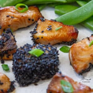 square crop of cod bites crusted with black sesame seeds garnished with green onions next to snap peas on a white plate.