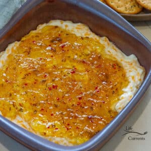 square crop looking down into a baking dish filled with pepper jelly topped cheese dip with crackers on the right.