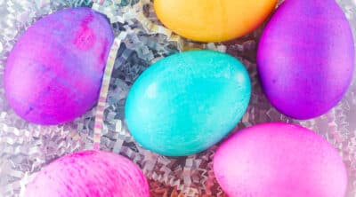 square crop of several richly dyed Easter eggs on white paper Easter grass.
