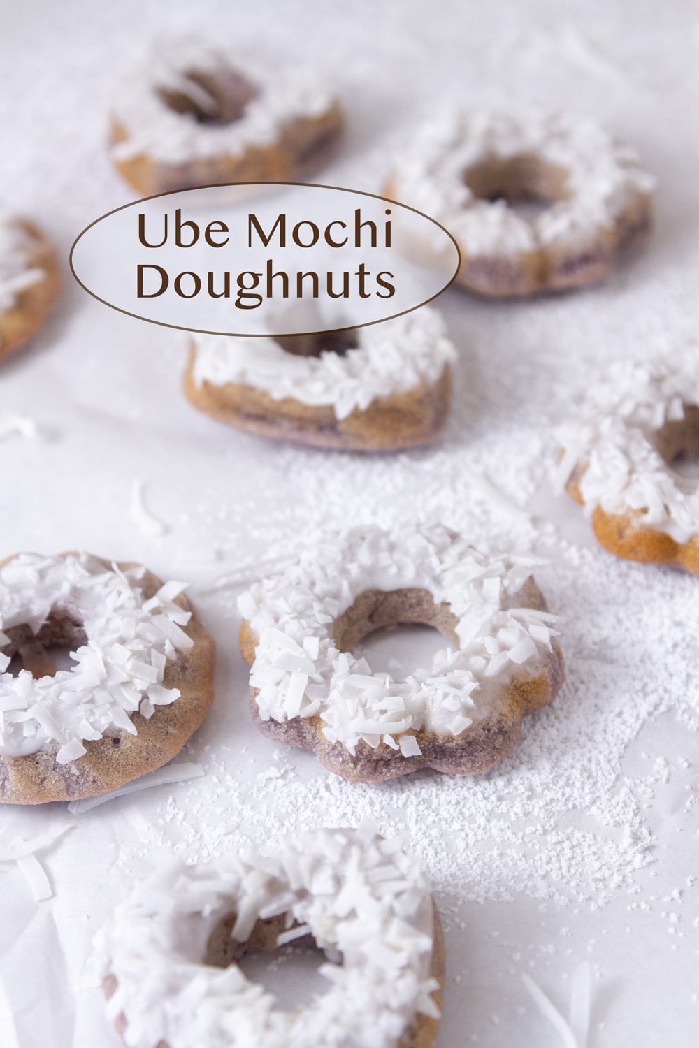 some ube mochi donuts glazed and with shredded coconut on top on a white parchment paper.