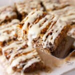 serving a slice of baked oatmeal on a metal server in front of the pan of oatmeal squares.