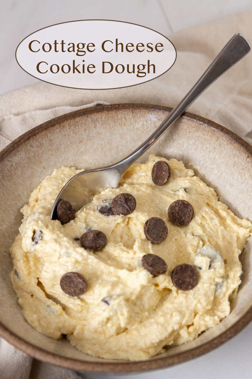 a white bowl filled with cookie dough and a spoon in it with chocolate chips on top of the dough.
