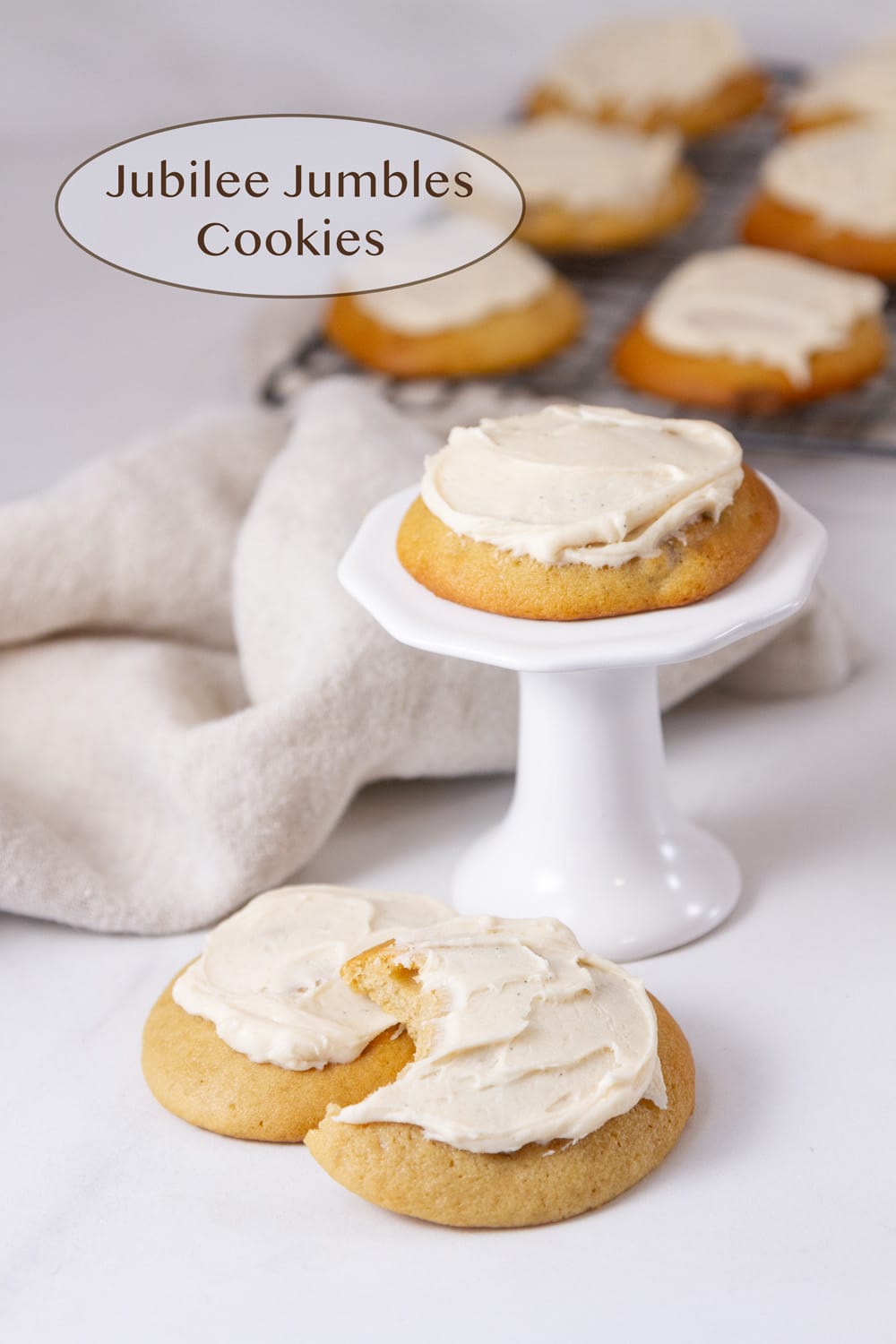 A cookie on a pedestal with two cookies in front of it and a wire rack of cookies in the background.