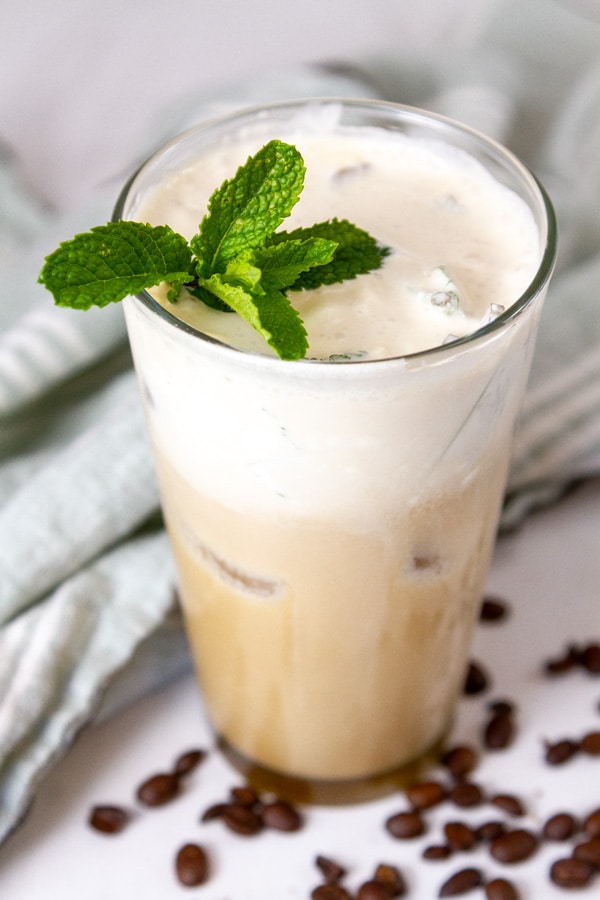 an iced mint mojito coffee with coffee beans around it and a green cloth in the background.