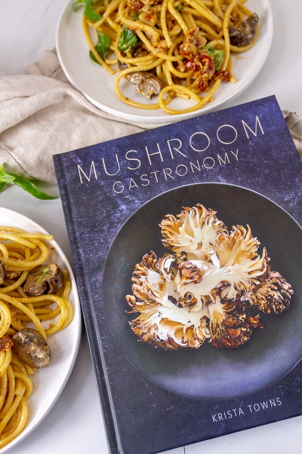 a cookbook next to two plates of pasta.