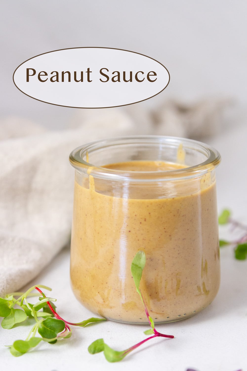 a glass jar filled with peanut sauce some sprouts and a cloth napkin around the jar.