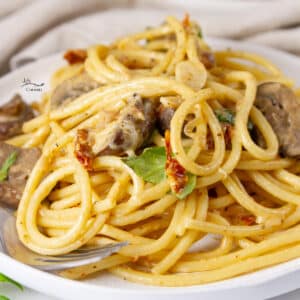 square crop of a plate of Creamy Mushroom Sun Dried Tomato Pasta with a fork on the left side.