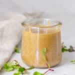 square crop of a glass jar with peanut sauce in it, sprouts and a cloth napkin around the jar.