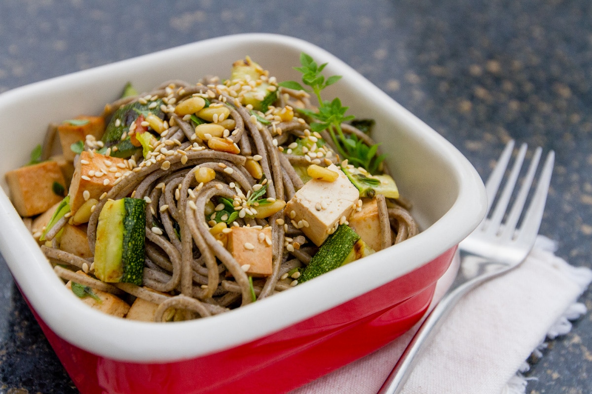 soba noodles with tofu and veggies in a red serving dish with a fork next to it.
