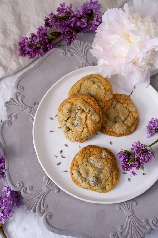 a white plate on a grey charger with cookies on the plate surrounded by flowers.