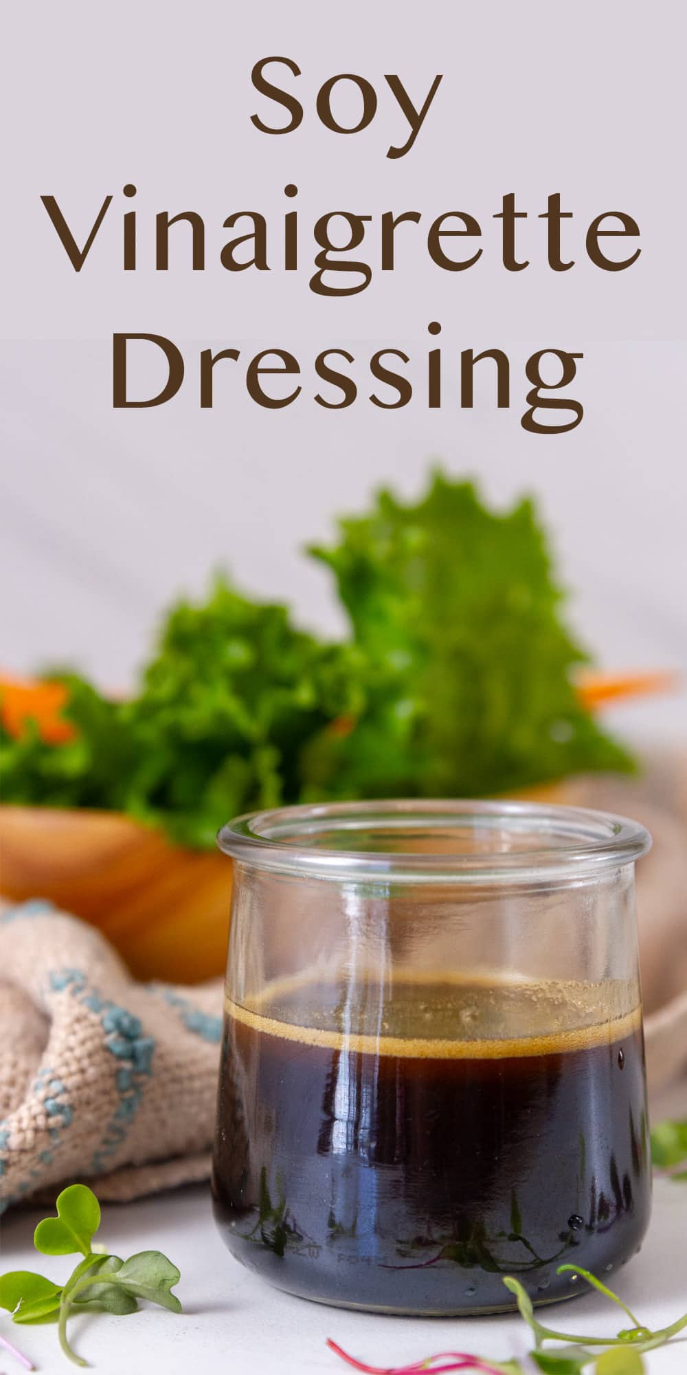 a small glass jar with dressing in it in front of a salad.