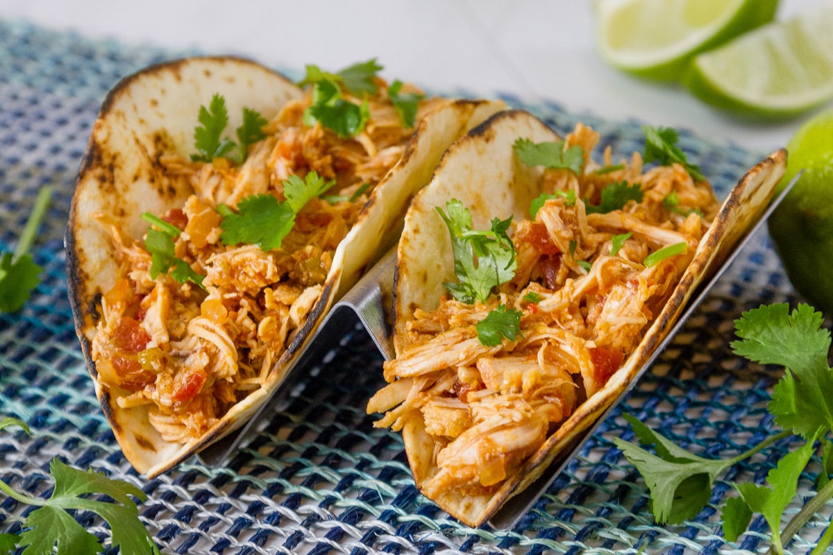 two chicken tacos on a blue mat with limes and cilantro around.