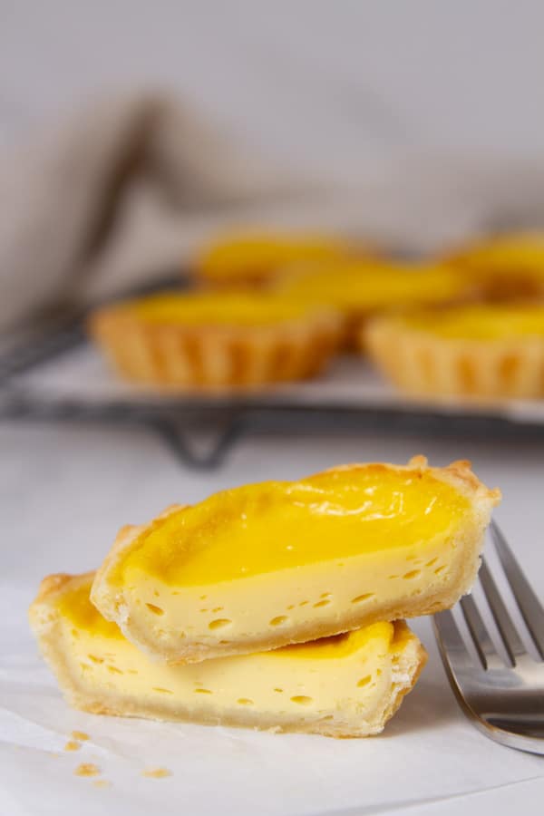 a tart that's been cut in half so you can see the inside next to a fork in front of tarts on a wire rack.