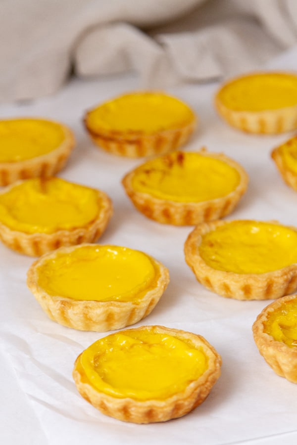 egg tarts on a piece of parchment paper with a cloth napkin in the background.