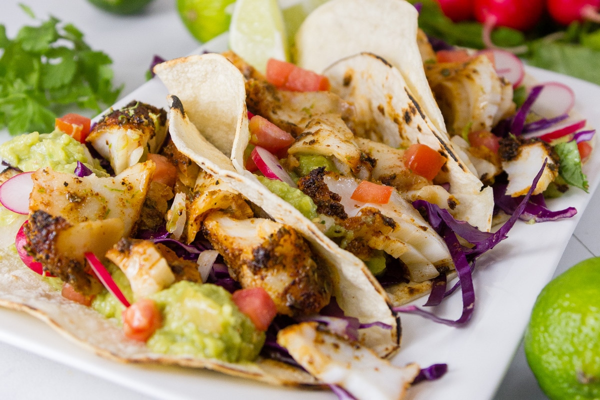 fish tacos on a white plate with limes.