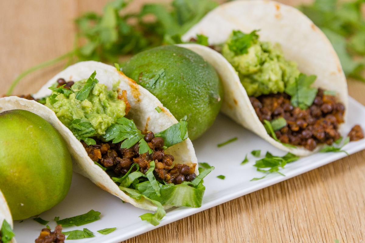 Two lentil tacos with limes in between on a white plate.