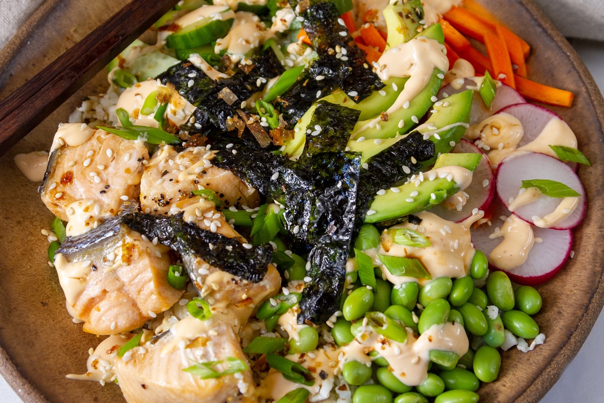 salmon, nori, edamame, carrots and radishes in a bowl with chopsticks on the side.
