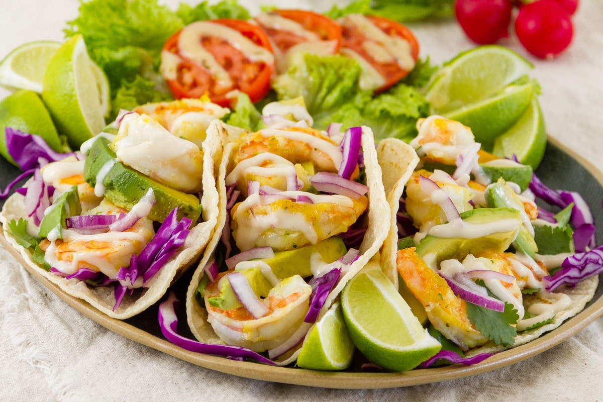three shrimp tacos on a plate with a salad behind it.