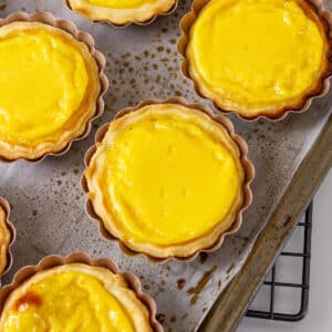 square crop of baked egg tarts on a baking sheet on a cooling rack.