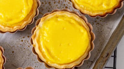 square crop of baked egg tarts on a baking sheet on a cooling rack.
