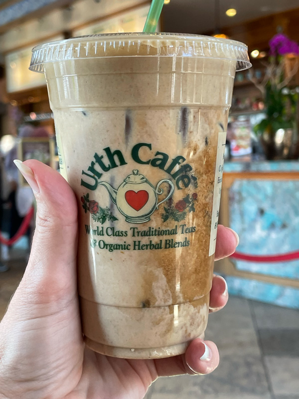 an iced coffee from Urth Caffe being held by a hand in front of their counter.