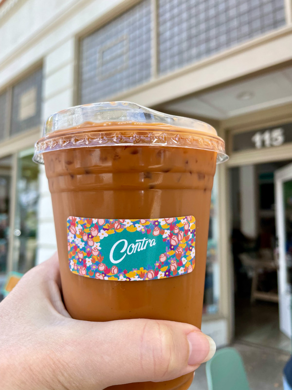 an iced coffee from Contra being held up in front of their shop.