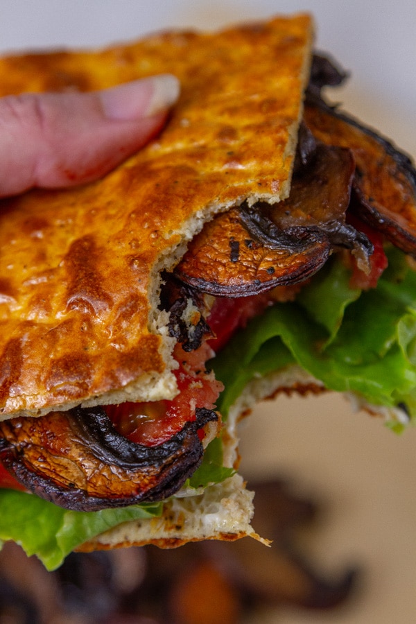 a mushroom bacon lettuce and tomato sandwich on cottage cheese bread with a bite out of it being held by a hand.