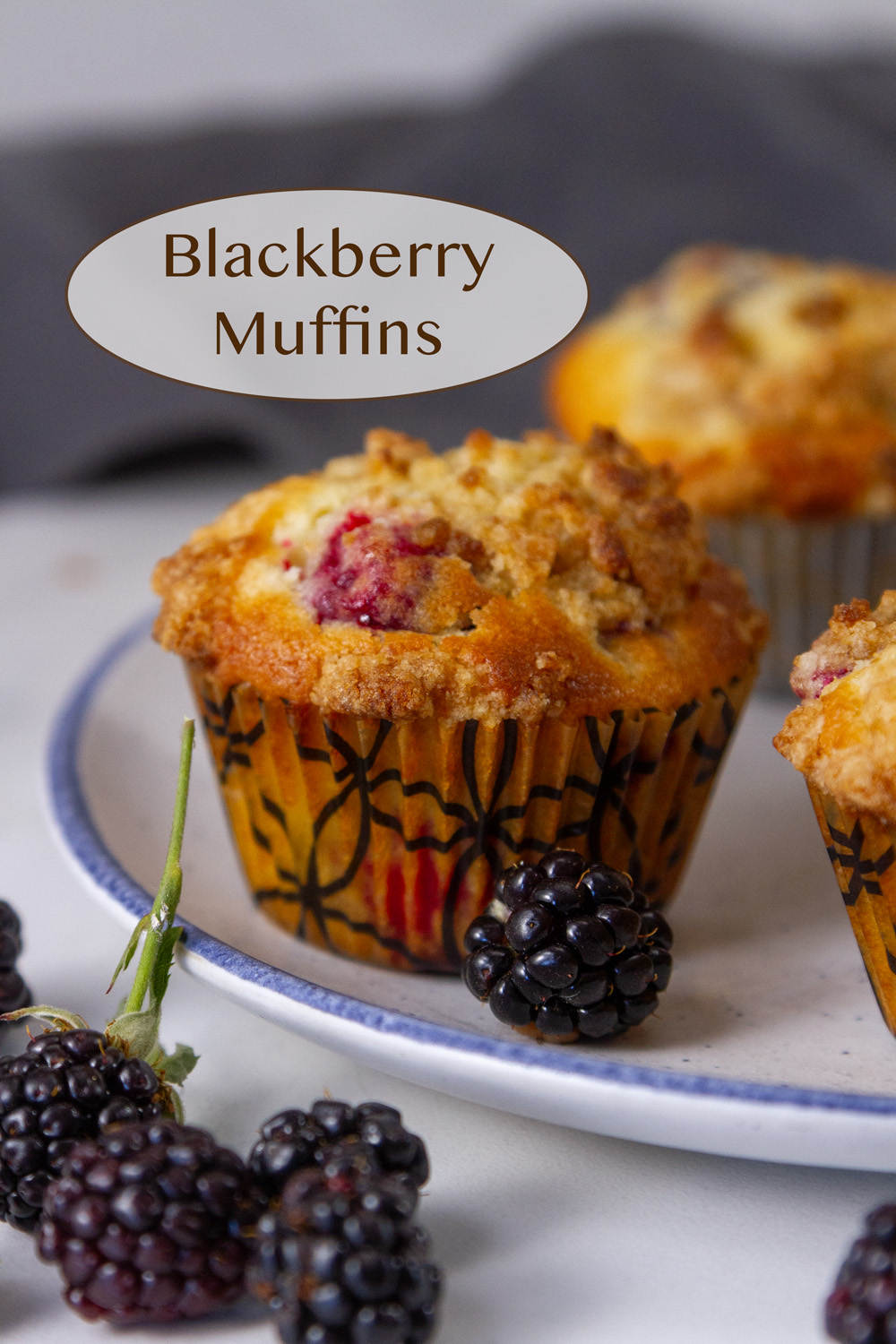 blackberry muffins on a plate with fresh blackberries around and a cloth napkin in the background.