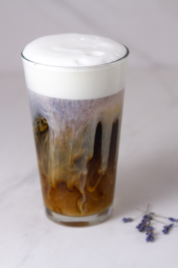 an iced coffee with cold foam and some dried lavender flowers next to it.