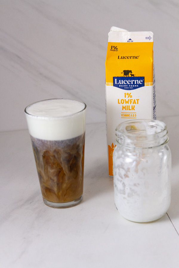 an iced coffee, a mason jar with milk in it, and a carton of 1% milk.