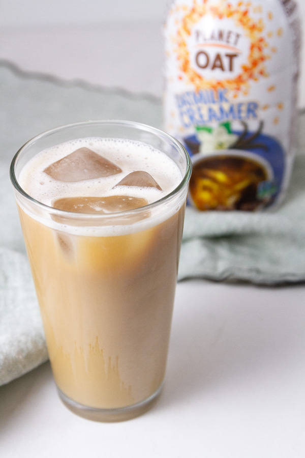 an iced coffee made with oatmilk creamer and the bottle of creamer is in the background.