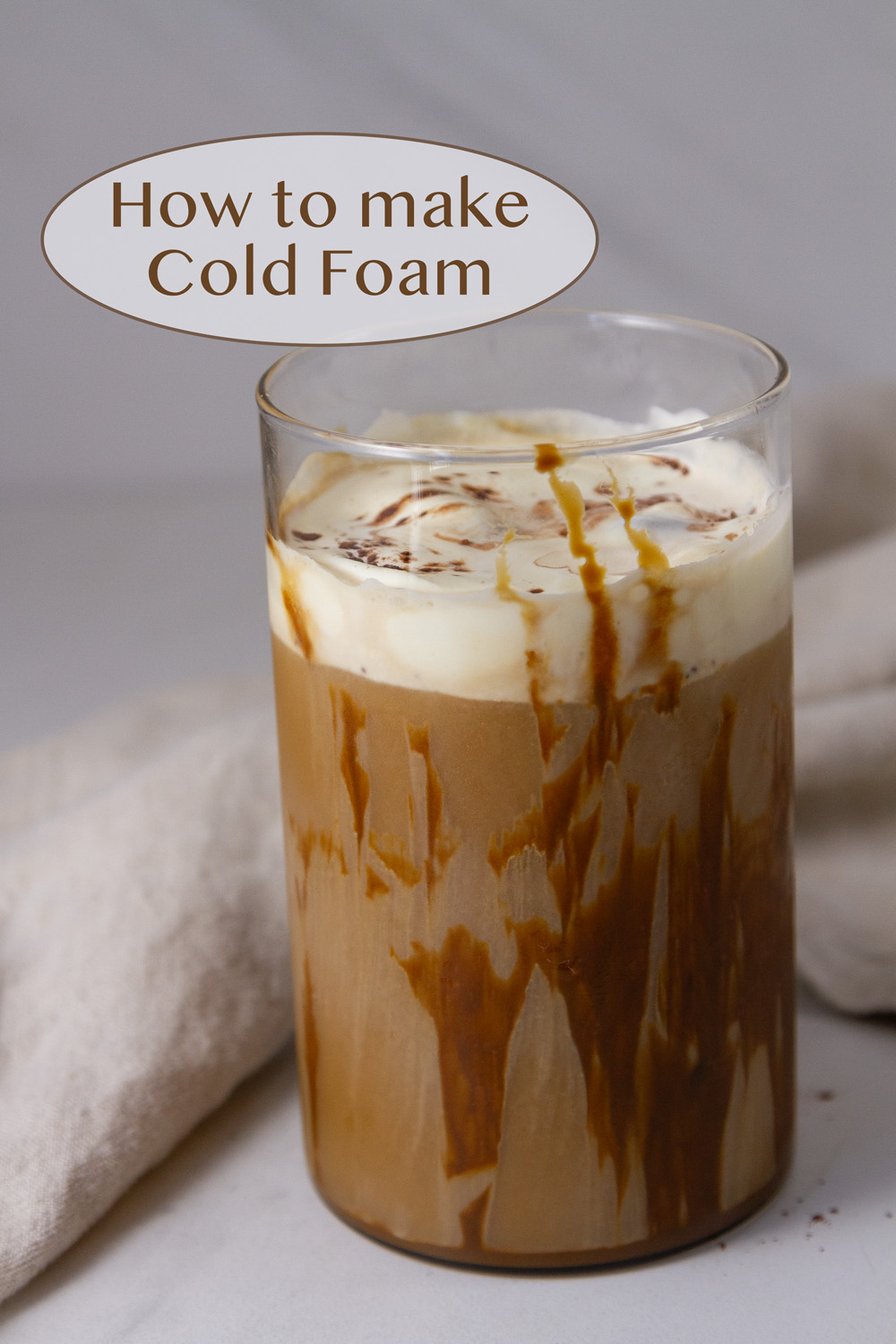 a glass of iced coffee topped with cold foam with a cloth napkin in the background.