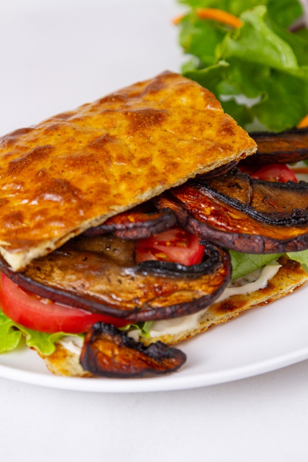 flatbread wrapped around mushrooms, tomato, lettuce on a white plate.