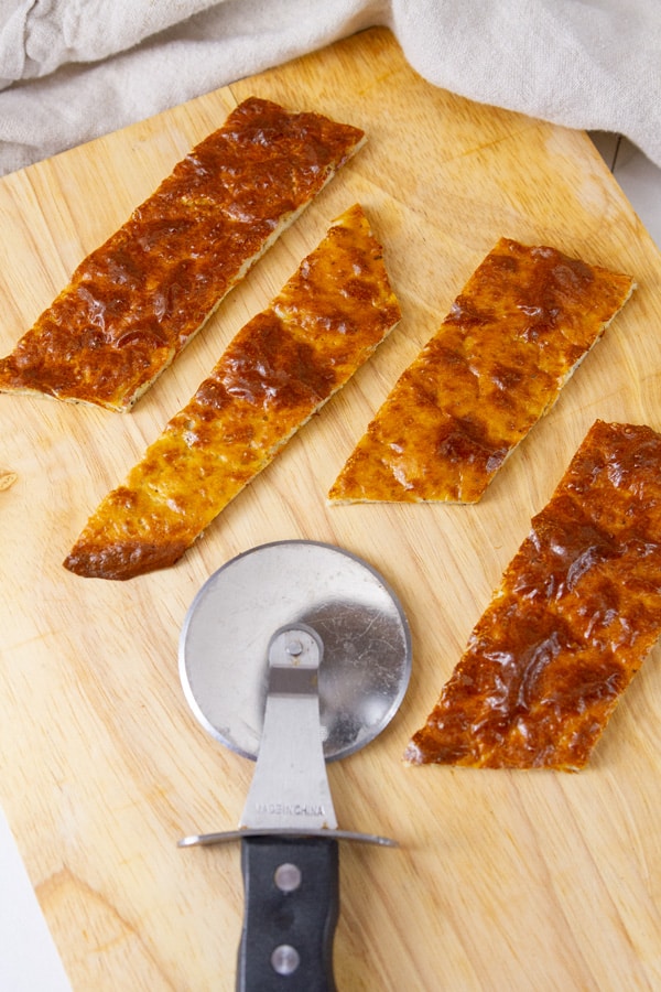 thin flatbread cut into small pieces on a wooden cutting board with a pizza wheel next to it.