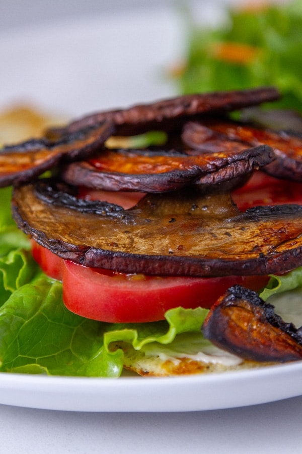 cooked mushrooms on top of sliced tomatoes, lettuce, and mayo on a piece of flatbread.