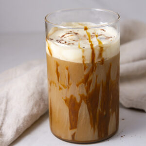 square crop of a glass of iced coffee with a mocha drizzle and a cloth napkin behind it.
