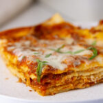 square crop of a slice of lasagna showing the layers and it's garnished with basil.