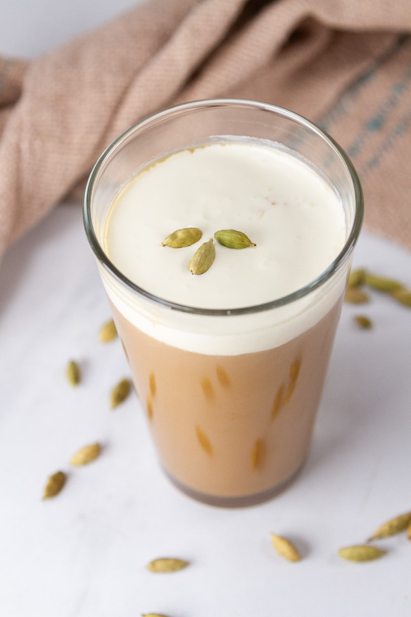 An iced cardamom latte topped with cold foam and garnished with cardamom pods.