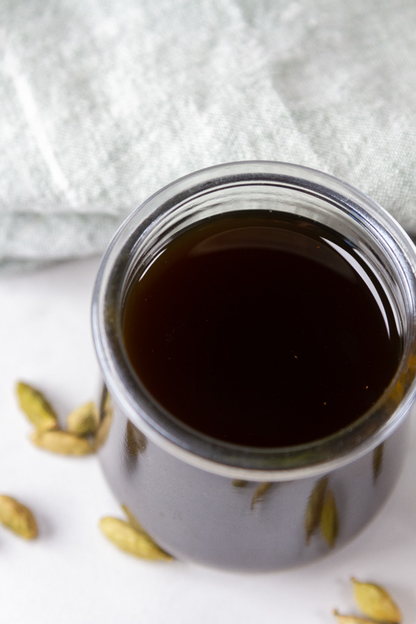 looking down into a glass jar with syrup in it and cardamom pods around it.