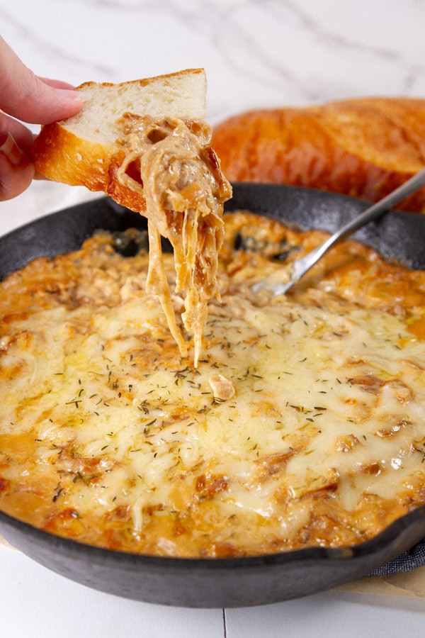 a piece of bread lifting the onion dip out of the skillet.
