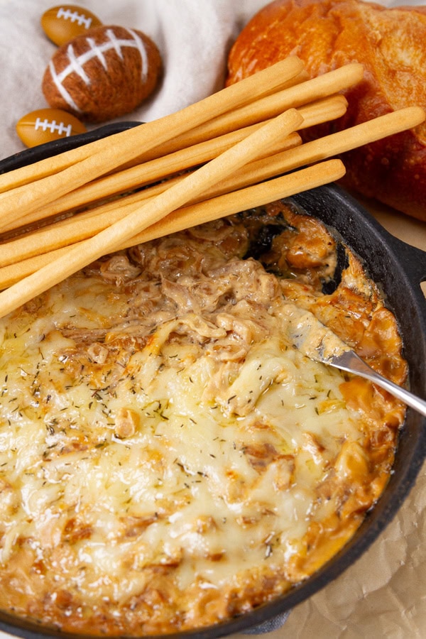 dip in a skillet with bread and Italian hard bread sticks around the skillet some small footballs in the upper left as well.