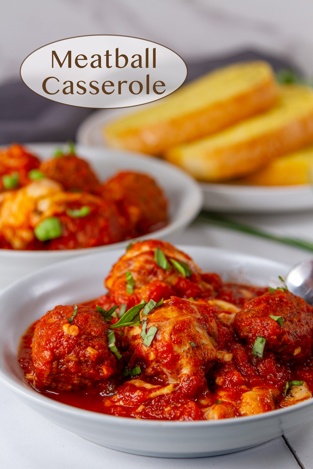 Two bowls with meatballs in red sauce with cheese and a plate of garlic bread in the background.