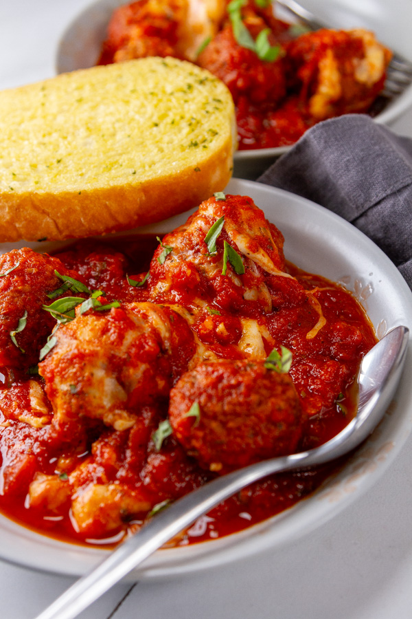 meatballs in marinara with a piece of garlic bread and a spoon in the bowl.