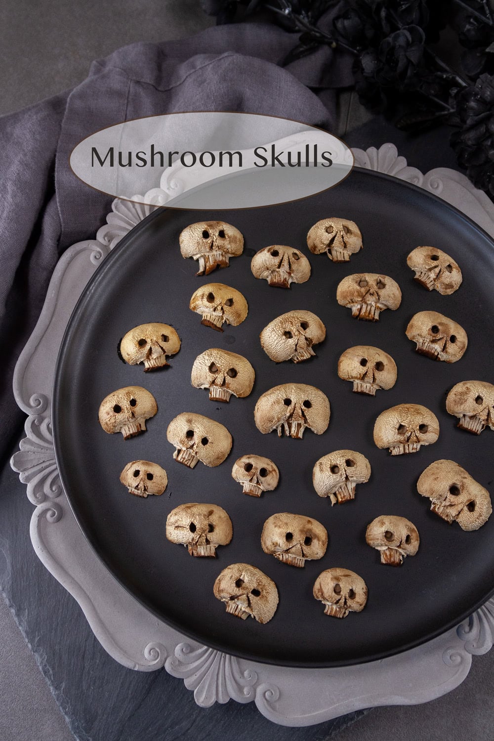white mushrooms carved to look like skulls all on a black plate with black flowers in the background.