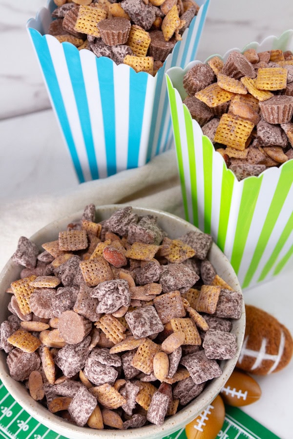 Two colorful tall square bowls filled with snack mix and a shorter bowl in front.