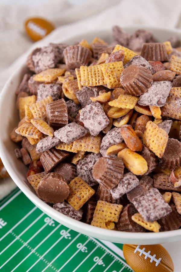 close up on chex mix in a white bowl with football decorations around it.