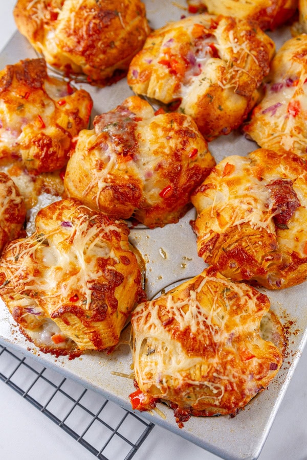 baked pizza muffin biscuits in a muffin tray on a wire cooling rack.