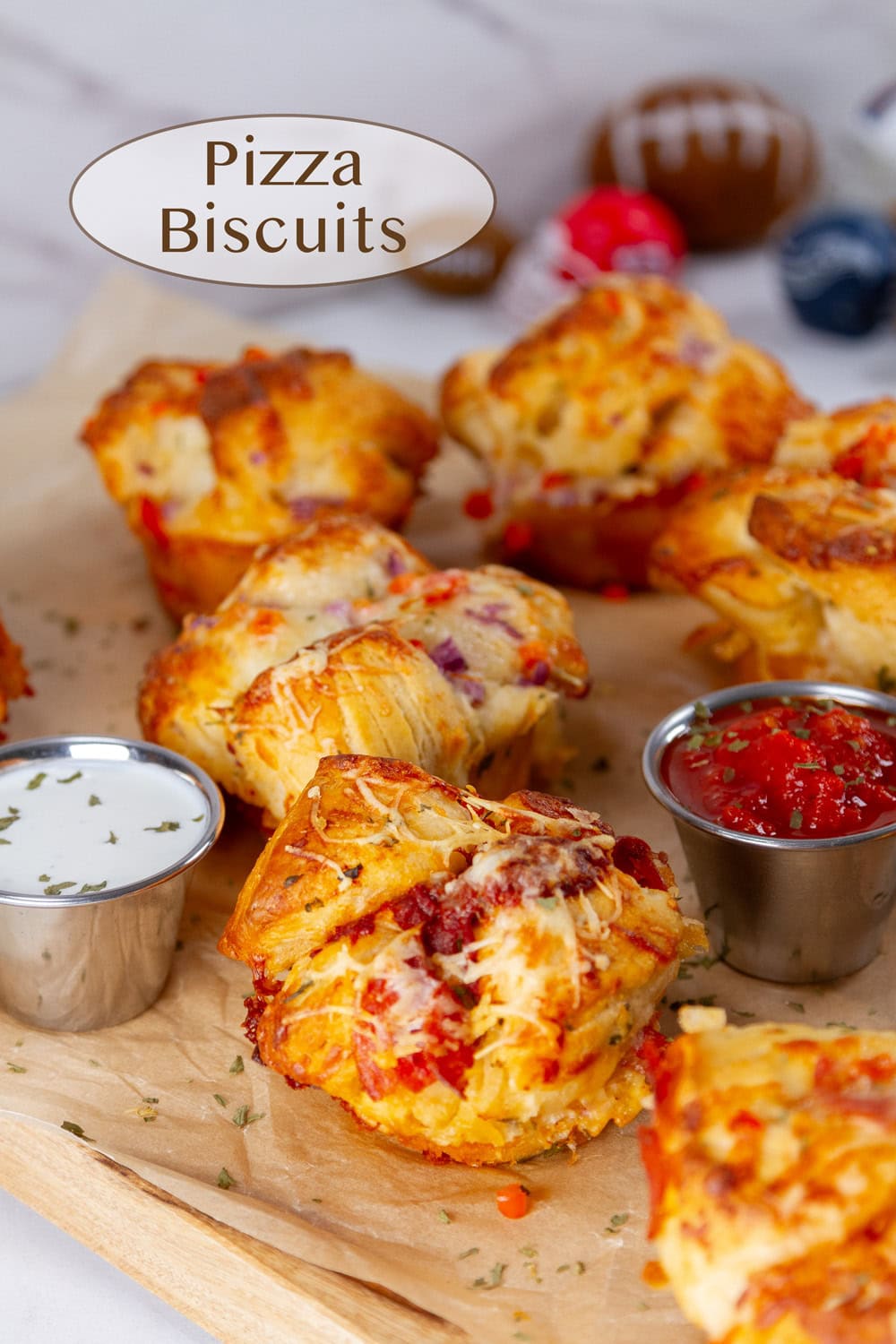 Pizza Biscuit muffins on a brown parchment paper with marinara and ranch for dipping in front of some play footballs.