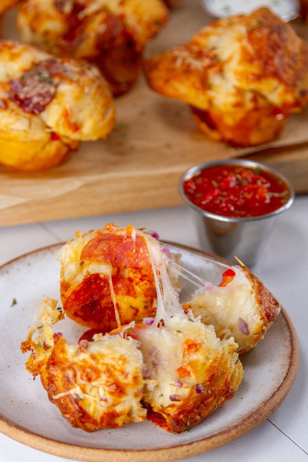 A wooden cutting board with pizza biscuits on it and one biscuit in in front of the tray and it's been pulled apart.
