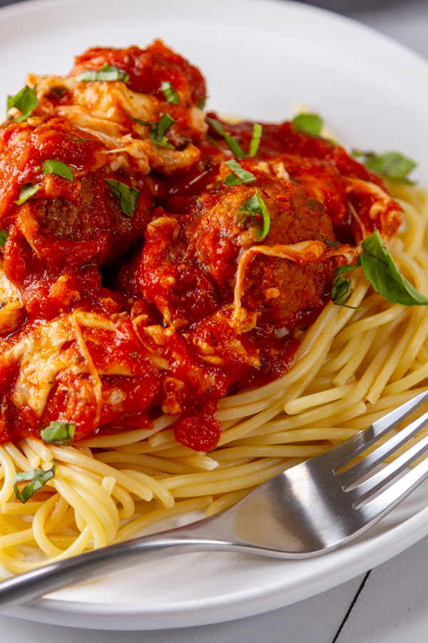 meatballs in spaghetti sauce with cheese over spaghetti pasta and a fork on the plate.